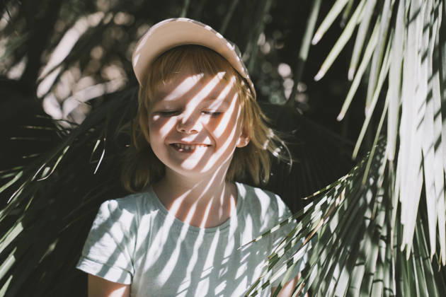 Playful child hiding behind palm leaves outdoors in sunlight model released, Symbolfoto, NDEF03045