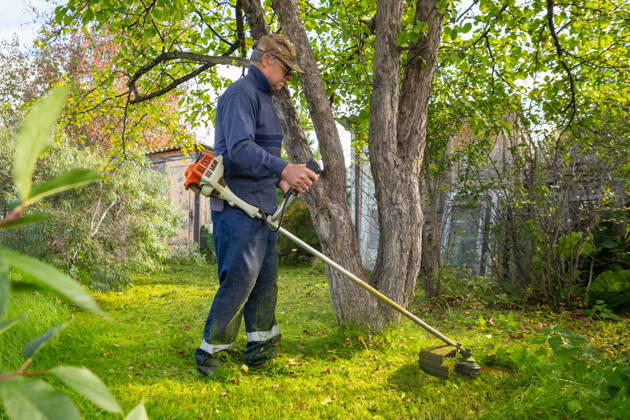 Senior man uses grass trimmer to cut overgrown lawn in his backyard Chelyabinsk, Chelyabinsk Oblast, Russia CR_STCJ260106-1921669-01 ,model released, Symbolfoto