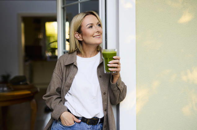 Smiling person with green smoothie standing on the patio at home model released, Symbolfoto property released, BSZF02945