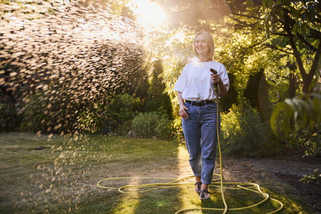 Smiling woman watering lawn with hose outdoors at sunset in summer model released, Symbolfoto property released, BSZF02960