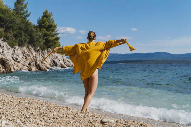 Woman in yellow cape enjoying playful moment by the sea on beach model released, Symbolfoto, NDEF03193