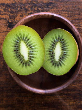 Kiwi-Frucht-Hälften in Holzschale, Draufsicht Top view of fresh green kiwi sliced in half inside a rustic wooden bowl, showing vibrant texture, seeds, and healthy tropical fruit concept. (License=RF) Copyright: xZoonar.com KellyxDengesx 24550538