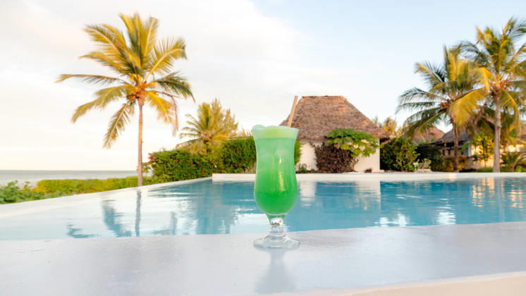 Honeymoon paradise at a Zanzibar resort pool A refreshing green cocktail by the pool at a luxurious Zanzibar resort. The serene background includes palm trees and a thatched villa, reflecting paradise. Model Released SilviaRedondo_ID33141_1127805_024 Copyright: xSilviaxRedondox RECORD DATE NOT STATED
