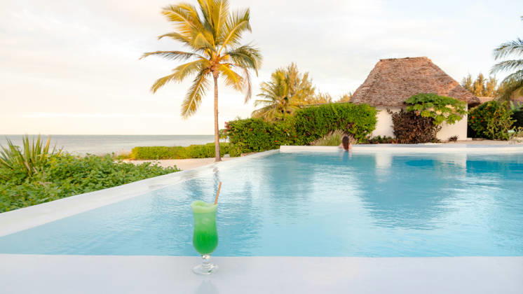 Honeymoon paradise at a Zanzibar resort pool A refreshing green cocktail by the pool at a luxurious Zanzibar resort. The serene background includes palm trees and a thatched villa, reflecting paradise. Model Released SilviaRedondo_ID33141_1127807_025 Copyright: xSilviaxRedondox RECORD DATE NOT STATED