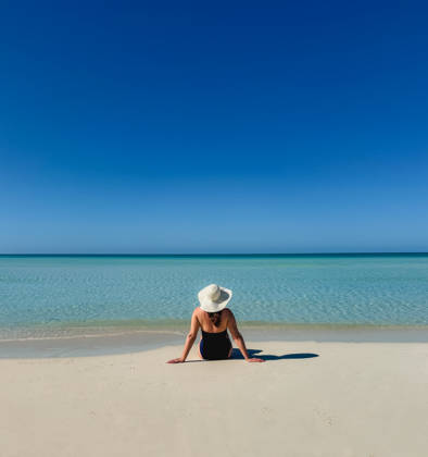Woman in swimsuit sunhat sitting on tropical beach looking at ocean. Grace Bay, Caicos Islands, Turks and Caicos Islands CR_DOHO26022882-1973352-01 ,model released, Symbolfoto