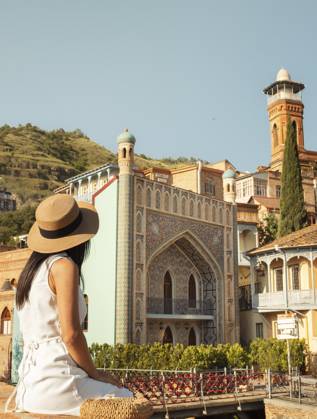 Frau sitzt im Sommerkleid mit Strohhut und bewundert die lebendige Architektur der Altstadt von Tiflis, Georgien. Traditionelle Holzbalkone, Moschee Minarett und historische Gebäude. Reisen, Sightseeing, Sommerurlaub Woman sit in summer dress straw hat admiring vibrant architecture old town Tbilisi, Georgia. Traditional wooden balconies, mosque minaret, and historic buildings. Travel, sightseeing, summer vacation Copyright: imageBROKER EvaldasxMikoliunas ibxemi16707968.jpg ,model released, Symbolfoto ,property released