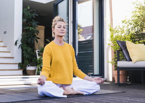 Woman meditating outdoors on sunny home terrace in yellow sweater model released, Symbolfoto property released, UUF36563