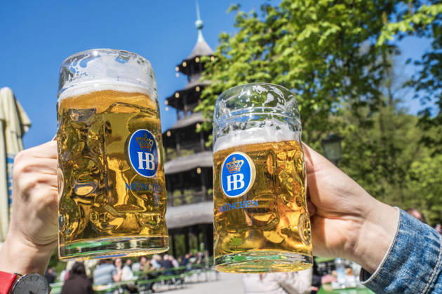 Beer garden at the Chinese Tower, spring day in the English Garden, two guests toast with their mugs of beer, Munich, April 2026 Germany, Munich, April 22, 2026, Beer garden at the Chinese Tower, spring in the English Garden, temperatures up to 16 degrees, many enjoy the sun with beer and a snack, two guests toast with their mugs, everythi