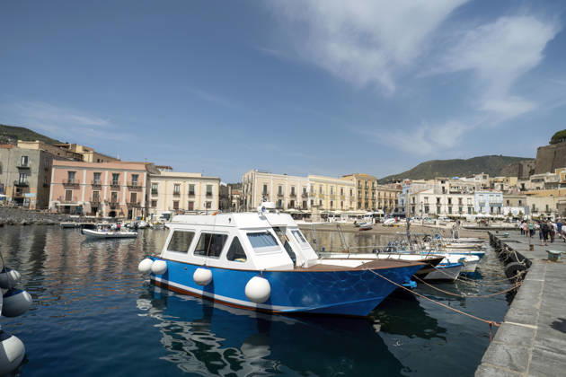 Ein traditionelles blau-weißes Fischerboot, das im Hafen von Mondello auf Sizilien vor Anker liegt. Bunte historische Gebäude säumen die Uferpromenade am Mittelmeer. Eine Szene aus einem italienischen Küstendorf. Traditional blue and white fishing boat moored in Mondello harbor, Sicily. Colorful historic buildings line the waterfront with Mediterranean Sea. Italian coastal village scene. (License=RF) Copyright: xZoonar.com ArpanxBhatiax 24973547