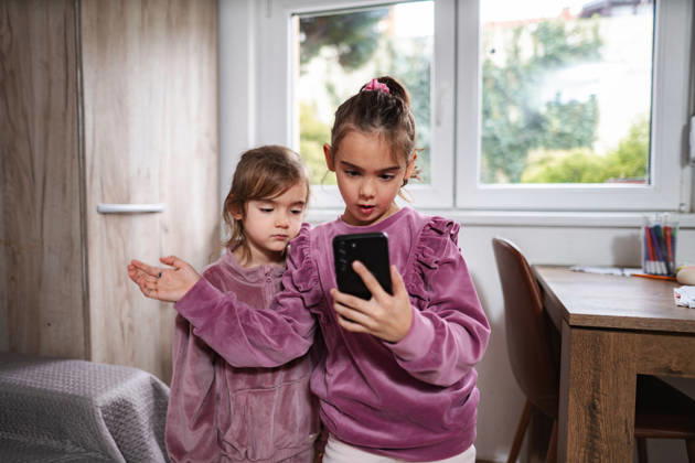 Zwei kleine Schwestern schauen sich gemeinsam in einem Kinderzimmer ein Smartphone an Little sisters sharing smartphone playing mobile game at home (License=RF) ,model released, Symbolfoto Copyright: xZoonar.com JelenaxCvetkovicx 24970275 ,model released, Symbolfoto ,property released