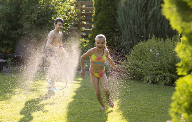 Glückliche Geschwister, die im Garten mit dem Gartenschlauch spielen und sich im sonnigen Hinterhof am Wasserspritzen erfreuen. Sommerzeit. Happy children brother and sister playing in the garden hose and having fun with spray of water in sunny backyard. Summer time. (License=RF) ,model released, Symbolfoto Copyright: xZoonar.com UliaxZotaninax 25041655 ,model released, Symbolfoto ,property released