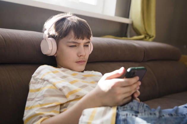 Ein Junge im Vorpubertätsalter sitzt zu Hause auf dem Sofa, hat Kopfhörer auf, hört Musik und schaut sich ein Video an. Seine Lieblingsmusik. Generation Z. preteen boy wearing headphones listens to music and watches a video sitting on the couch at home. favorite music. Generation Z. (License=RF) ,model released, Symbolfoto Copyright: xZoonar.com UliaxZotaninax 25046862 ,model released, Symbolfoto ,property released