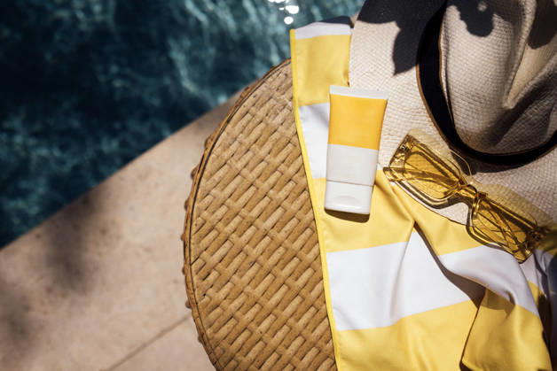 Eine Sommerszene am Pool mit einem Strohhut, einer gelben Sonnenbrille, Sonnencreme und einem gestreiften Strandtuch auf einem geflochtenen Tisch in der Nähe eines glitzernden blauen Pools Poolside arrangement includes a straw hat, yellow sunglasses, sunscreen, and a striped towel on a woven table beside a clear blue swimming pool (License=RF) Copyright: xZoonar.com DashaxPetrenkox 25102896