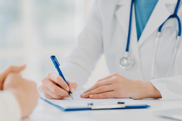 Arzt in weißem Kittel mit Stethoskop, der während einer Patientenberatung am Schreibtisch in der Arztpraxis auf einem Klemmbrett notiert Doctor in white coat with stethoscope writing on clipboard during patient consultation at medical office desk (License=RF) ,model released, Symbolfoto Copyright: xZoonar.com ViorelxKurnosovx 25131479 ,model released, Symbolfoto ,property released