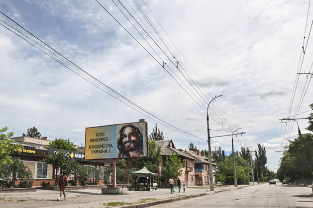 RECORD DATE NOT STATED A billboard reading Jesus is risen — Ukraine will rise again stands on a street in the frontline city of Kherson, Ukraine, on June 2, 2026. The Russian army attacks the city daily with FPV drones and other unmanned aerial vehicles, deliberately terrorizing civilians. Russian forces conduct hunts for local residents, tracking them with FPV drones and dropping explosives. Police officers, medics, public transport, and urban infrastructure are also targeted. Based on the intensity of attacks, Kherson is informally divided into yellow and red zones, with the red zone considered the most dangerous due to constant shelling and drone strikes. Anti-drone netting has been installed above roads to help protect against Russian FPV drone atta Copyright: xDmytroxSmolienkox