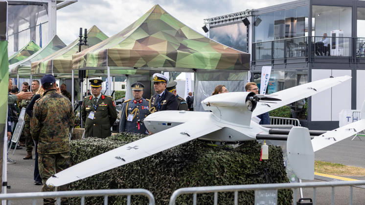 Trade visitor day at ILA Berlin 2026, Berlin, 12 06 2026 Military officers from various nations inspect an unmanned reconnaissance drone UAV with Bundeswehr markings on an open-air exhibition stand The drone is presented on a camouflage net base, in the background pavilions in spot camouflage Schöneberg Berlin ExpoCenter Airport Brandenburg Germany 20260612-286A9572-M4000