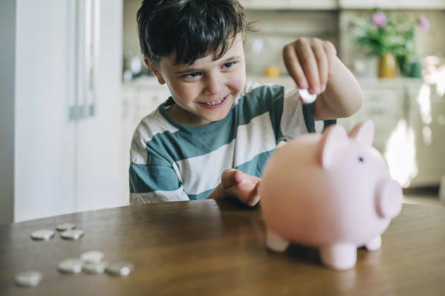 A smiling boy puts a coin into a pink piggy bank at home model released, Symbolfoto property released, ANAF06326