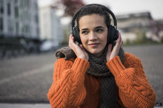 Portrait of woman wearing scarf and orange knit pullover outdoors listening music with cordless headphones model released, Symbolfoto, MOEF01878