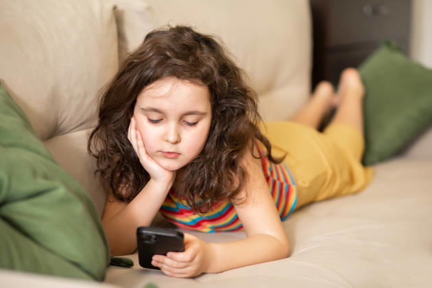 Ein süßes kleines Mädchen, das mit seinem Smartphone spielt, liegt zu Hause auf dem Sofa im Wohnzimmer Bored and sad cute little girl using smart phone lies on sofa in living room at home. (License=RF) ,model released, Symbolfoto Copyright: xZoonar.com ZulfiiaxIshmukhametovax 25315774 ,model released, Symbolfoto ,property released