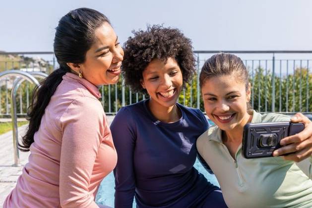 Diverse female friends posing for selfie poolside in long-sleeve athletic tops holding smartphone, model released, property released, 26.08.2025 06:00:00, 7967313 Copyright: xIDS-260501_2xcreatorid:x0x 7967313