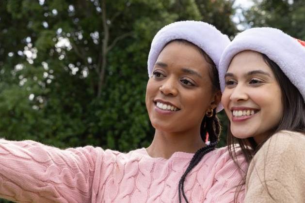 Diverse female friends posing for selfie in park, holding phone and wearing Santa hats, sweaters, model released, property released, 14.08.2025 06:00:00, 7811321 Copyright: xIDS-260426xcreatorid:x0x 7811321