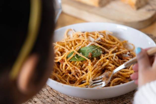 Child holding fork with turquoise nails, twirling spaghetti with basil in white bowl at table, model released, property released, 03.07.2025 06:00:00, 6981104 Copyright: xIDS-260427_1xcreatorid:x0x 6981104