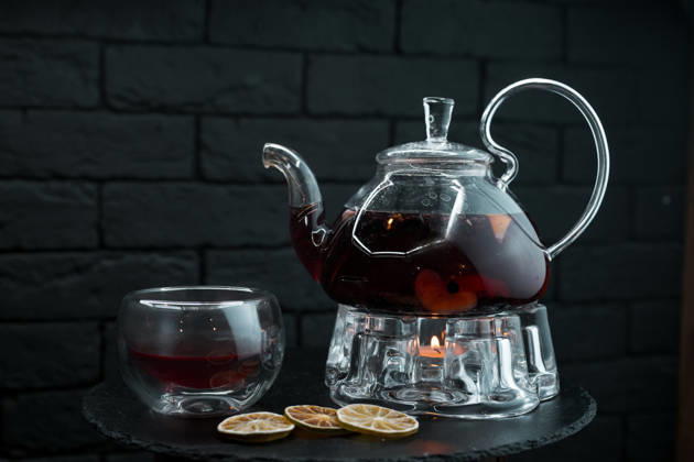 Schwarzer Aromatic Herbal tea with Minzblättern and Ginger and Oranges and Fruit slices in a antique Glass teapot next to a Glass cup at a Wooden table in a cafÃ Beautiful Tea service a Tea 1102838702