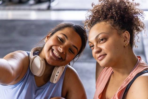 Diverse female friends posing for selfie in gym wearing athletic tops white headphones gold hoops, model released, property released, 19.08.2025 06:00:00, 7853528 Copyright: xIDS-260521_3xcreatorid:x0x 7853528