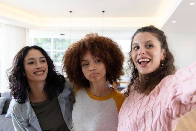 Diverse female friends posing for selfie, smiling, holding smartphone in bright living room sofa, model released, property released, 02.09.2025 06:00:00, 8093909 Copyright: xIDS-260407xcreatorid:x0x 8093909