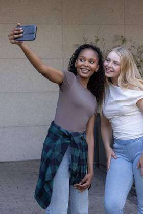 Diverse female friends posing for selfie, leaning toward smartphone by tiled wall with plaid shirt, model released, 30.10.2025 06:00:00, 9109305 Copyright: xIDS-260605_3xcreatorid:x0x 9109305