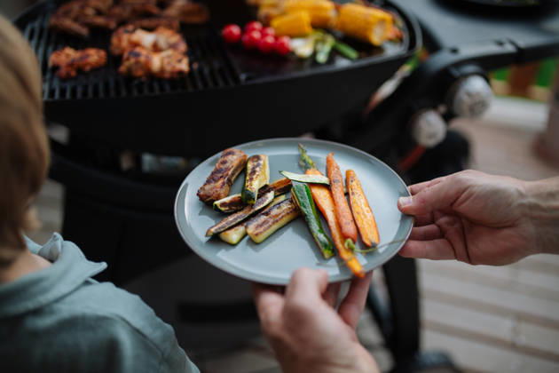 Father putting grilled meat and vegetable on plate to his son during family summer garden party. A father putting grilled meat and vegetable on plate to his son during family summer garden party. model released