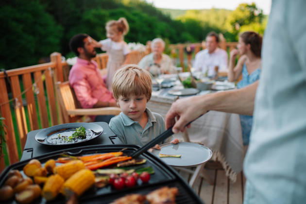 Father putting grilled meat and vegetable on plate to his son during family summer garden party. A father putting grilled meat and vegetable on plate to his son during family summer garden party. model released