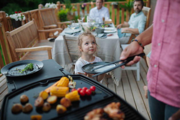 Father putting grilled meat and vegetable on plate to his son during family summer garden party. A father putting grilled meat and vegetable on plate to his son during family summer garden party. model released