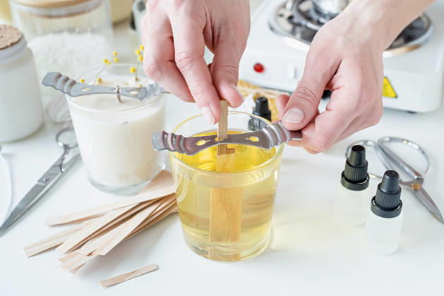 Nahaufnahme einer Frau, die den Holzdocht in eine handgemachte Kerze steckt Creative hobby of candle making at home. Woman making decorative aroma candle at table, setting wooden wick into glass with melted soy wax (License=RF) Copyright: xZoonar.com ILONAxSHOROKHOVAx 25393609