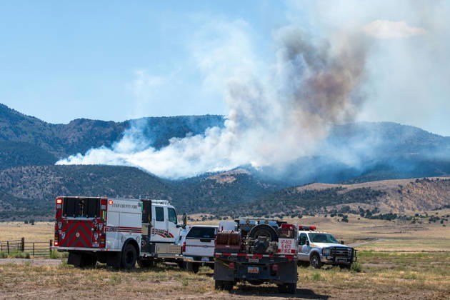 August 23, 2026, Elberta, Utah, USA: A plume of thick smoke rises into the sky above a mountain ridge as the Big Mountain Fire burns southwest of Elberta, Utah, United States, on August 23, 2026. A line of emergency response vehicles can be seen staged along a dirt road below the active wildland blaze. Elberta USA - ZUMAm292 20260823_znp_m292_002 Copyright: xCharlesxMcClintockxWilsonx