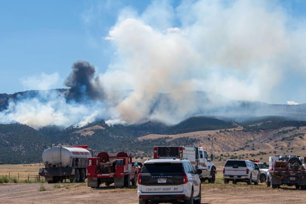 August 23, 2026, Elberta, Utah, USA: A plume of thick smoke rises into the sky above a mountain ridge as the Big Mountain Fire burns southwest of Elberta, Utah, United States, on August 23, 2026. A line of emergency response vehicles can be seen staged along a dirt road below the active wildland blaze. Elberta USA - ZUMAm292 20260823_znp_m292_004 Copyright: xCharlesxMcClintockxWilsonx
