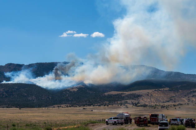 August 23, 2026, Elberta, Utah, USA: A plume of thick smoke rises into the sky above a mountain ridge as the Big Mountain Fire burns southwest of Elberta, Utah, United States, on August 23, 2026. A line of emergency response vehicles can be seen staged along a dirt road below the active wildland blaze. Elberta USA - ZUMAm292 20260823_znp_m292_007 Copyright: xCharlesxMcClintockxWilsonx
