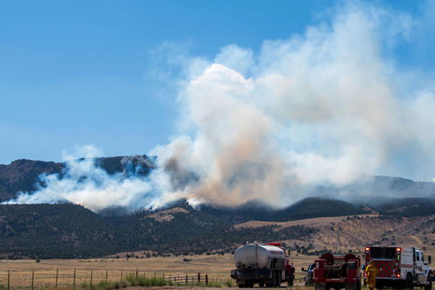 August 23, 2026, Elberta, Utah, USA: A plume of thick smoke rises into the sky above a mountain ridge as the Big Mountain Fire burns southwest of Elberta, Utah, United States, on August 23, 2026. A line of emergency response vehicles can be seen staged along a dirt road below the active wildland blaze. Elberta USA - ZUMAm292 20260823_znp_m292_005 Copyright: xCharlesxMcClintockxWilsonx