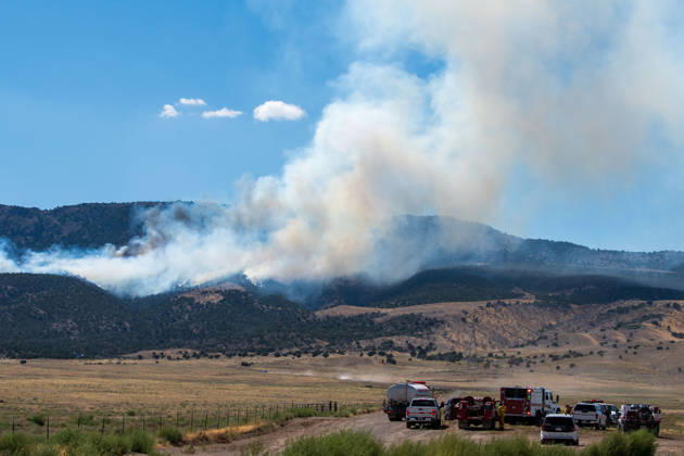 August 23, 2026, Elberta, Utah, USA: A plume of thick smoke rises into the sky above a mountain ridge as the Big Mountain Fire burns southwest of Elberta, Utah, United States, on August 23, 2026. A line of emergency response vehicles can be seen staged along a dirt road below the active wildland blaze. Elberta USA - ZUMAm292 20260823_znp_m292_009 Copyright: xCharlesxMcClintockxWilsonx