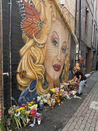 A woman arranges flowers at a memorial under a mural of Dolly Parton in Konxville, Tennessee on Friday, August 28, 2026.  TEN20260828101 AARONxJOSEFCZYK