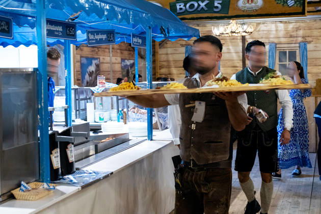 Augsburg, Bavaria, Germany - August 28, 2026: Opening of the Plärrer in Augsburg. A waiter wearing lederhosen carries several plates of food through the festival tent at the Augsburg Herbstplärrer. The festival food vendors provide meals to the numerous visitors at the folk festival