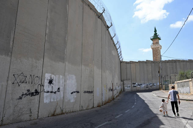 Palestinians walk beside the Israeli separation wall cutting off the citizens of Abu Dis from reaching East Jerusalem, without passing through a time consuming checkpoint, on Sunday, August 30, 2026. Thousands of Palestinian residents of East Jerusalem are forced to go through checkpoints to reach their schools, jobs, hospitals and visit family because of the separation wall.  JER2026083002 DEBBIExHILL