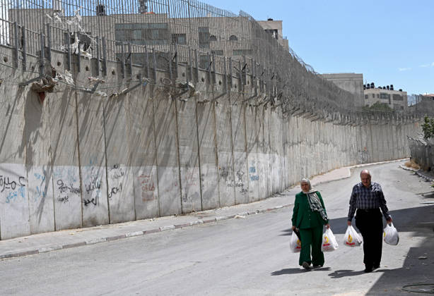 Palestinians carry groceries beside the Israeli separation wall that cuts through Beit Hanina in East Jerusalem on Sunday, August 30, 2026. Thousands of Palestinian residents of East Jerusalem are forced to go through time consuming checkpoints to reach their schools, jobs, hospitals and visit family because of the separation barrier.  JER2026083004 DEBBIExHILL