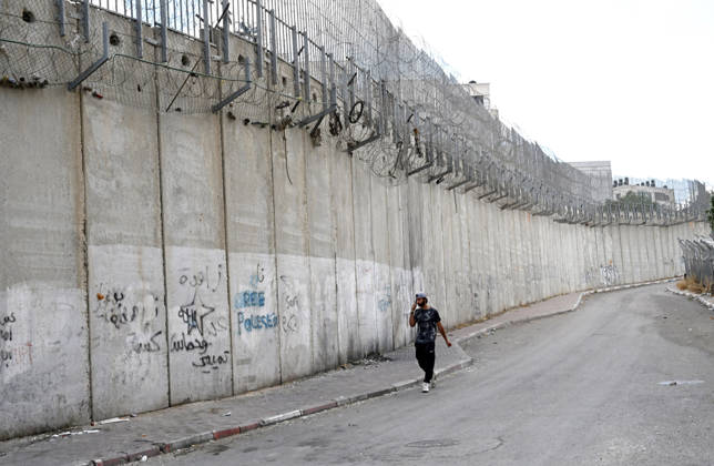 A Palestinian walks beside the Israeli separation wall that cuts through Beit Hanina in East Jerusalem on Sunday, August 30, 2026. Thousands of Palestinian residents of East Jerusalem are forced to go through time consuming checkpoints to reach their schools, jobs, hospitals and visit family because of the separation barrier.  JER2026083005 DEBBIExHILL