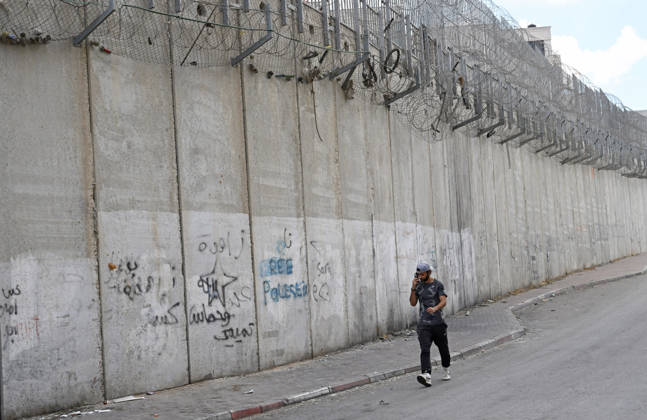 A Palestinian talks on a cellphone beside the Israeli separation wall that cuts through Beit Hanina in East Jerusalem on Sunday, August 30, 2026. Thousands of Palestinian residents of East Jerusalem are forced to go through time consuming checkpoints to reach their schools, jobs, hospitals and visit family because of the separation barrier.  JER2026083006 DEBBIExHILL