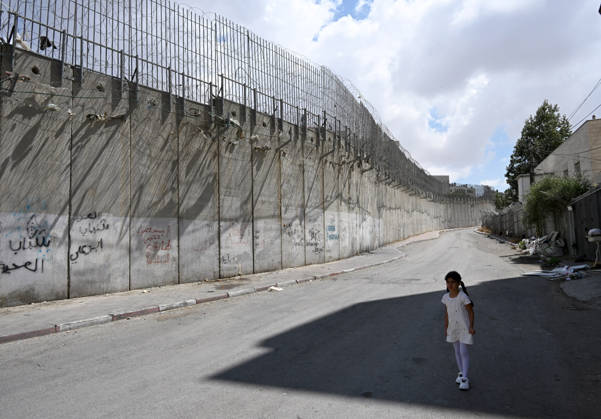 A Palestinian girl stands in the shade beside the Israeli separation wall that cuts through Beit Hanina in East Jerusalem on Sunday, August 30, 2026. Thousands of Palestinian residents of East Jerusalem are forced to go through time consuming checkpoints to reach their schools, jobs, hospitals and visit family because of the separation barrier.  JER2026083007 DEBBIExHILL
