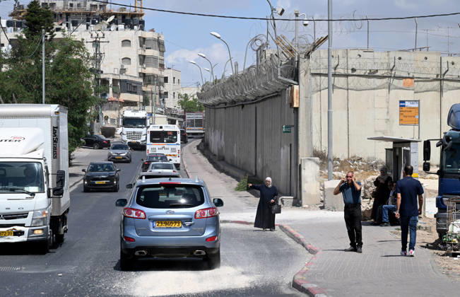 A Palestinian woman tries to flag a ride beside the Israeli separation wall that cuts through Beit Hanina in East Jerusalem on Sunday, August 30, 2026. Thousands of Palestinian residents of East Jerusalem are forced to go through time consuming checkpoints to reach their schools, jobs, hospitals and visit family because of the separation barrier.  JER2026083010 DEBBIExHILL
