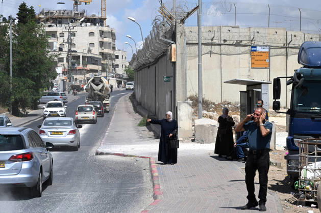 A Palestinian woman tries to flag a ride near the Israeli separation wall that cuts through Beit Hanina in East Jerusalem on Sunday, August 30, 2026. Thousands of Palestinian residents of East Jerusalem are forced to go through time consuming checkpoints to reach their schools, jobs, hospitals and visit family because of the separation barrier.  JER2026083011 DEBBIExHILL