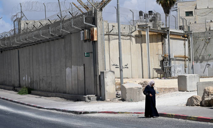 A Palestinian woman stands near the Israeli separation wall that cuts through Beit Hanina in East Jerusalem on Sunday, August 30, 2026. Thousands of Palestinian residents of East Jerusalem are forced to go through time consuming checkpoints to reach their schools, jobs, hospitals and visit family because of the separation barrier.  JER2026083012 DEBBIExHILL