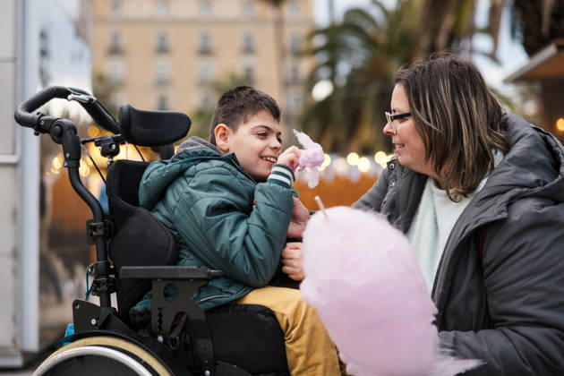 Mother and son in wheelchair eat cotton candy at outdoor market, JMIF00152